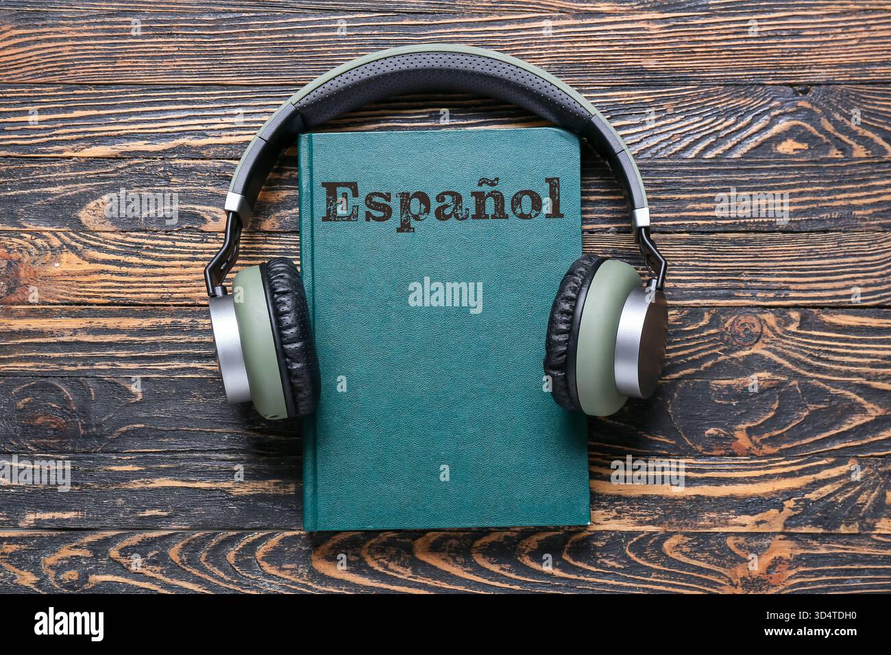 Buch und moderne Kopfhörer auf hölzernem Hintergrund. Konzept des Lernens Spanisch Stockfoto