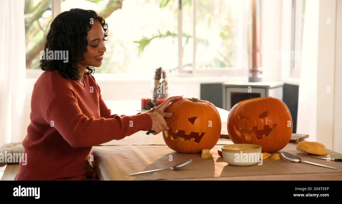 Schnitzende Frau in rostfarbenem Strickpullover, der zu Hause zwei Jack-o'-Laternen formt, mit Schnitzwerkzeugen Stockfoto