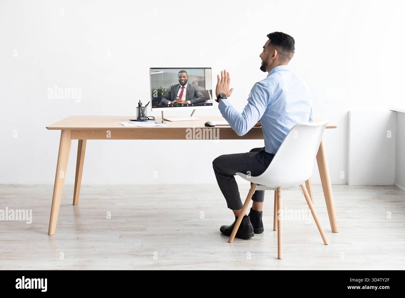 Junger Arabischer Geschäftsmann Winkt Während Eines Videoanrufs Die Hand, Während Er Vom Büro Aus Arbeitet Stockfoto
