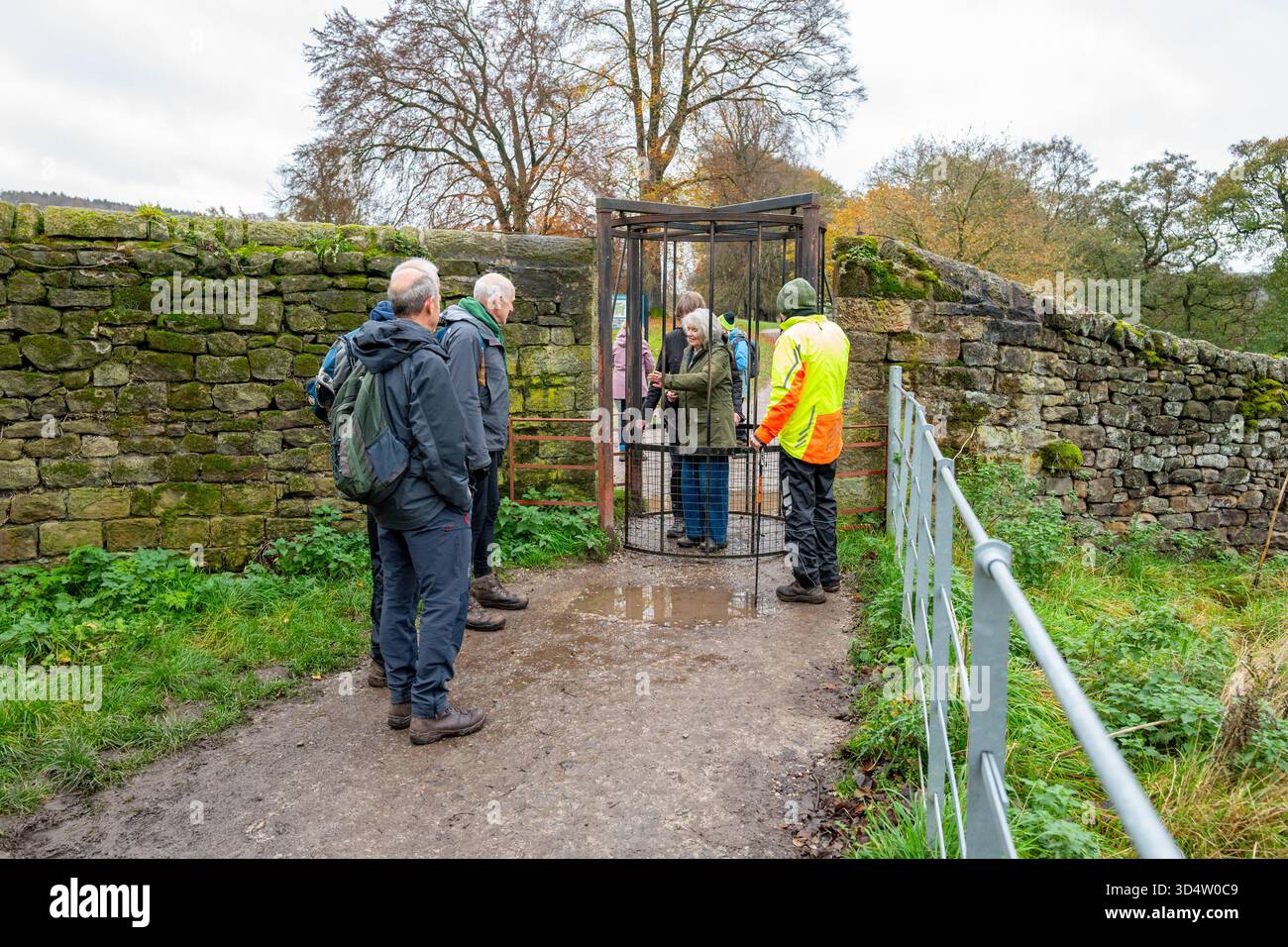 Männliche und weibliche Erwachsene Walker fahren an nassen und kalten Tagen über ein rotierendes Metalltor entlang eines Fußwegs. Stockfoto