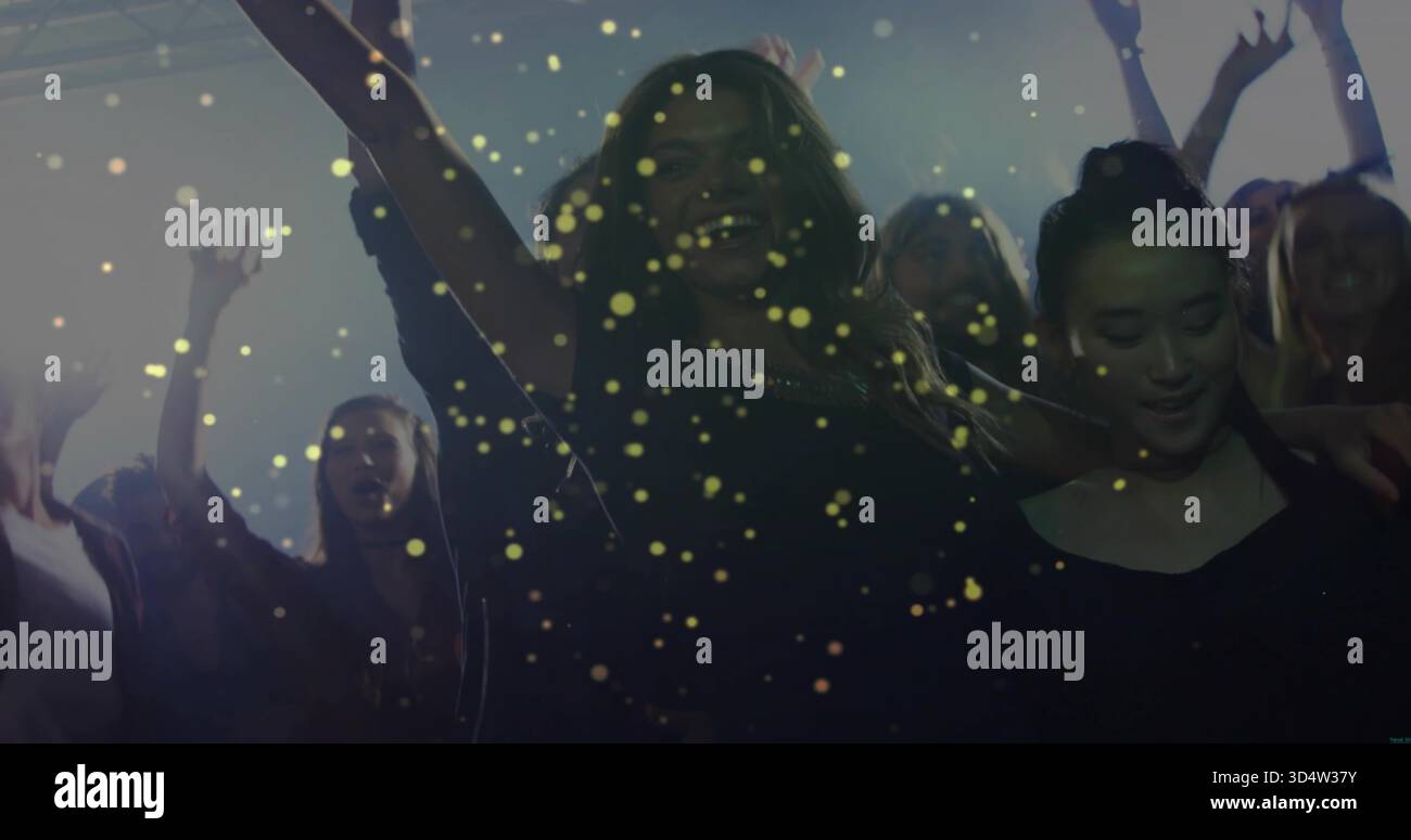 Tanzende Menge in dunkler Clubkleidung und Armlehnen auf dem Clubboden, goldenem Konfetti und Spotlights Stockfoto