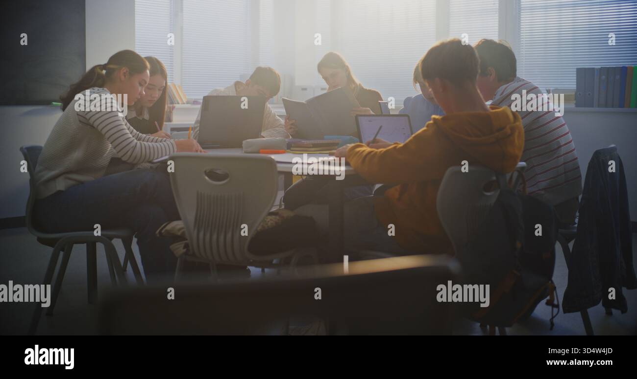 Schüler arbeiten an Laptops in hellen Klassenzimmern zusammen. Der Junge setzt sich an den Tisch und tritt Teamwork bei. Konzeptgruppenprojektarbeit und wesentliche Rolle des digitalen Lernens in der modernen Bildungsumgebung. Stockfoto