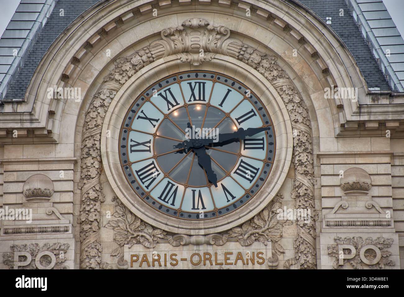 Die monumentale Uhr des Musée d'Orsay hebt sich in der Mitte der Fassade hervor, mit römischen Ziffern und einem in Stein gehauenen skulpturalen Rahmen. Stockfoto