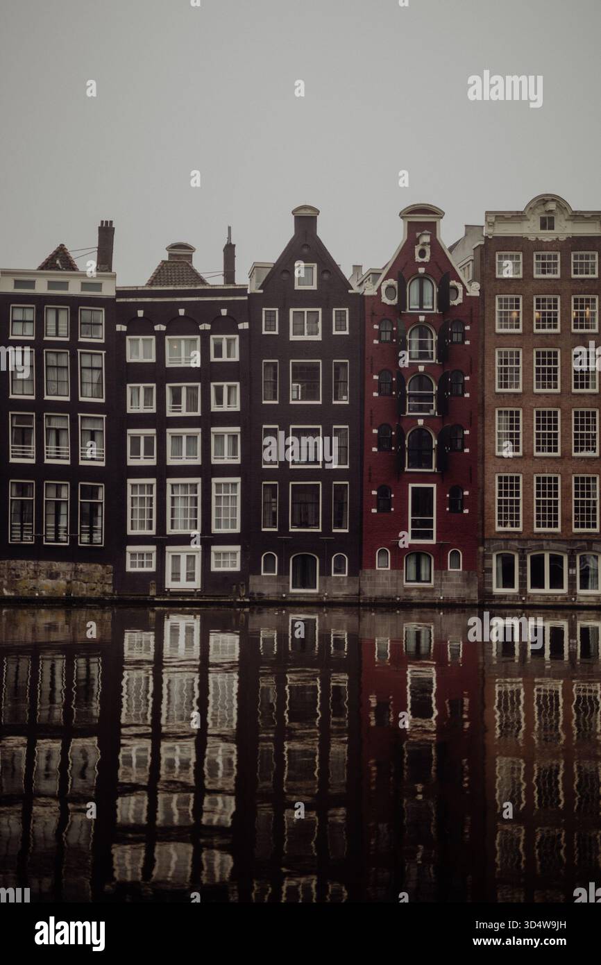 Nebeliger Morgen in Amsterdam mit Kanalhäusern und historischen Fassaden, die sich im ruhigen Wasser spiegeln, stimmungsvolle Stadtlandschaft Stockfoto