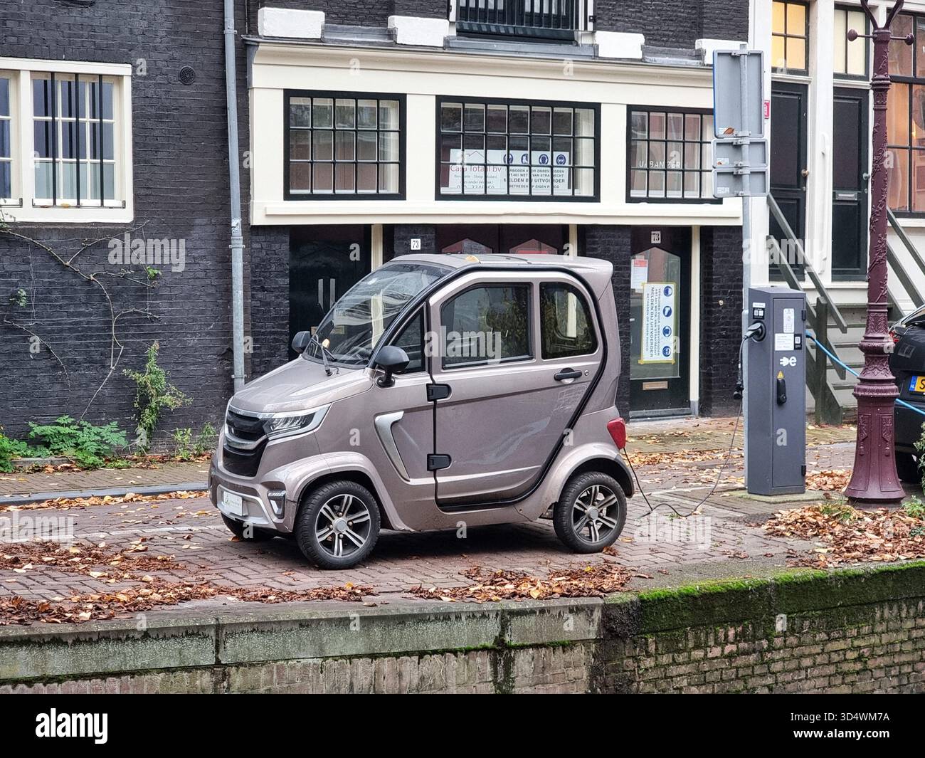 Elektrofahrzeug, Motion Mirage E-Car-Mikroauto, Citycar, Ladeanschluss am Rande des Kanals in Amsterdam, Niederlande - Smartphone-aufgenommenes Stockfoto