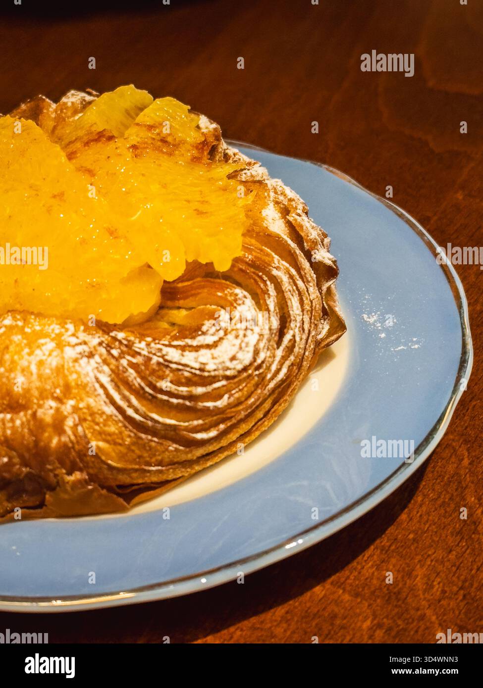 Köstliches goldbraunes dänisches Gebäck, das mit Puderzucker bestäubt ist, großzügig mit glänzenden kandierten Orangenscheiben belegt, serviert auf einem zarten hellen B Stockfoto