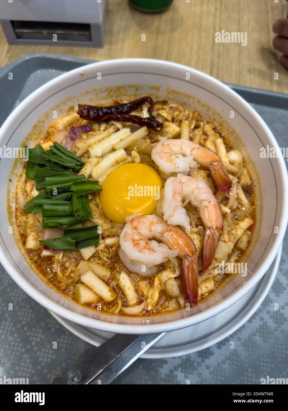 Eine lebendige Schüssel mit würzigen thailändischen Nudeln mit prallen Garnelen, einem reichhaltigen rohen Eigelb, duftenden Kräutern und feurigen getrockneten Chilis. Dieses tröstende, f Stockfoto