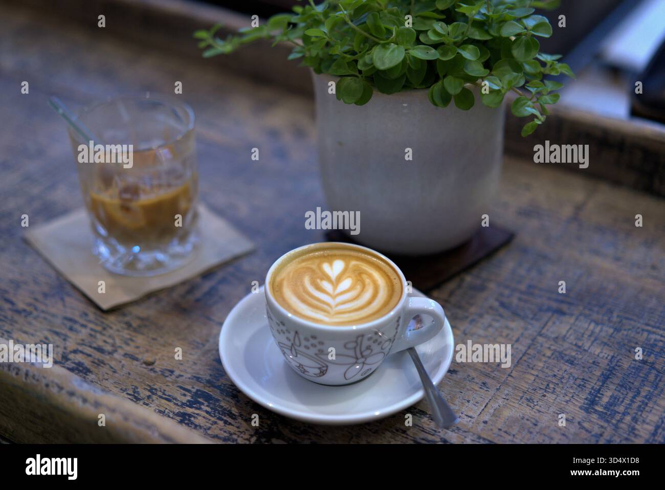 Cremige Latte Art in einem gemütlichen Café mit einem erfrischenden Glas Eiskaffee und einer kleinen Pflanze Stockfoto
