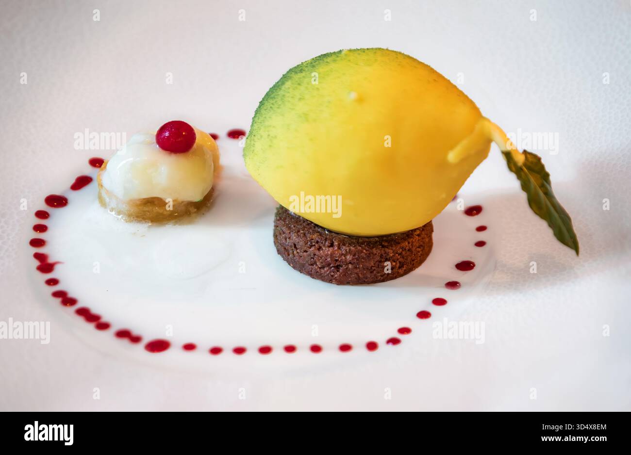 Gourmet-Dessert aus weißer Schokolade in Form einer Zitrone, gefüllt mit Vanilleeis, sitzt auf einer Schokoladenbasis mit Beerensoße-Dots in Nizza, Frankreich Stockfoto