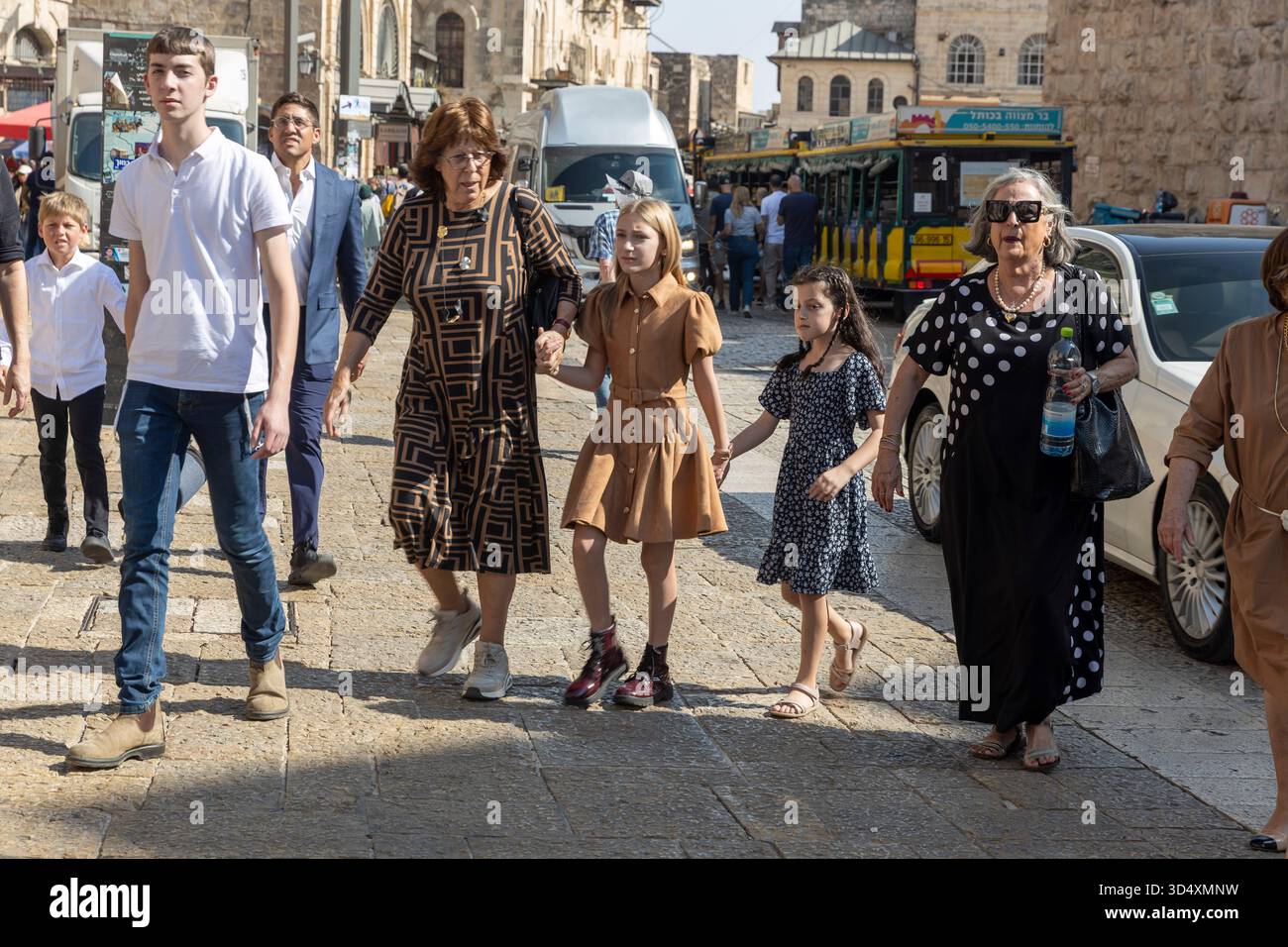 jerusalem, Israel, 2. November 2025, Eine mehrgenerationenübergreifende Familiengruppe, zu der Großmütter und Kinder gehören, die eine sonnenbeschienene Kopfsteinpflasterstraße n hinunterläuft Stockfoto
