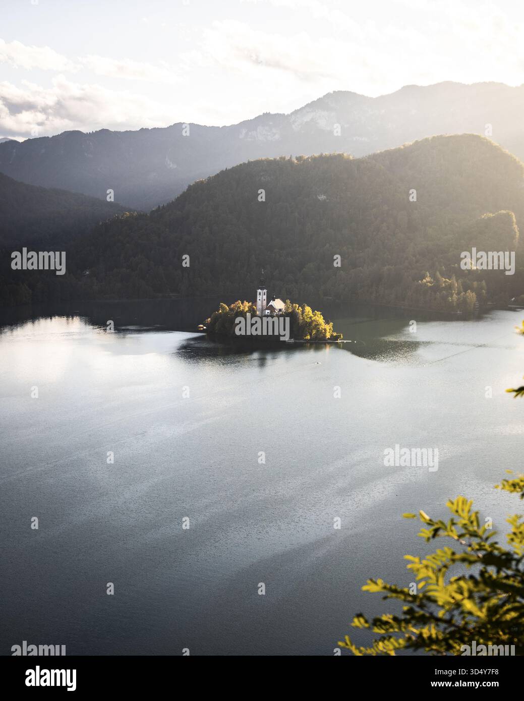 Blick auf eine Insel mit einer Kirche inmitten eines Sees, umgeben von Hügeln und üppigen Bäumen, Bled, Radovljica, Slowenien. Stockfoto