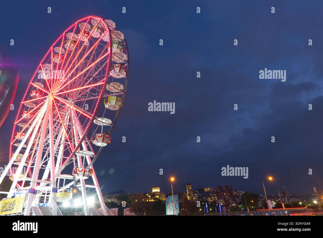 Eine dramatische Nachtszene mit einem hell beleuchteten Riesenrad, das überwiegend in leuchtendem Rot leuchtet. Das statische Erscheinungsbild des Rades (oder sehr langsame Bewegung Stockfoto
