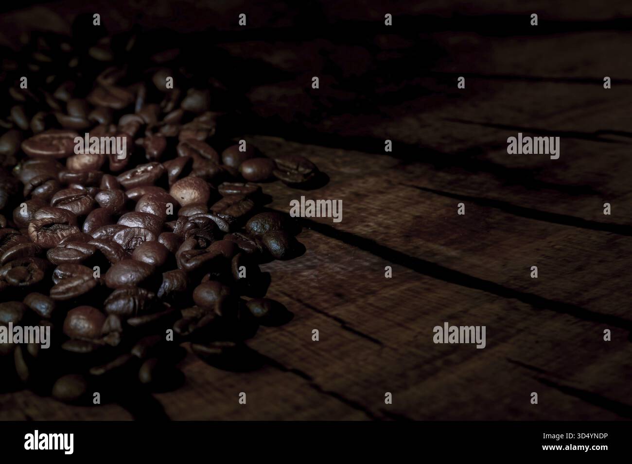 Dunkel geröstete Kaffeebohnen schaffen eine reiche Textur auf einem alten rustikalen Holztisch mit stimmungsvollen Schatten und warmem Licht Stockfoto