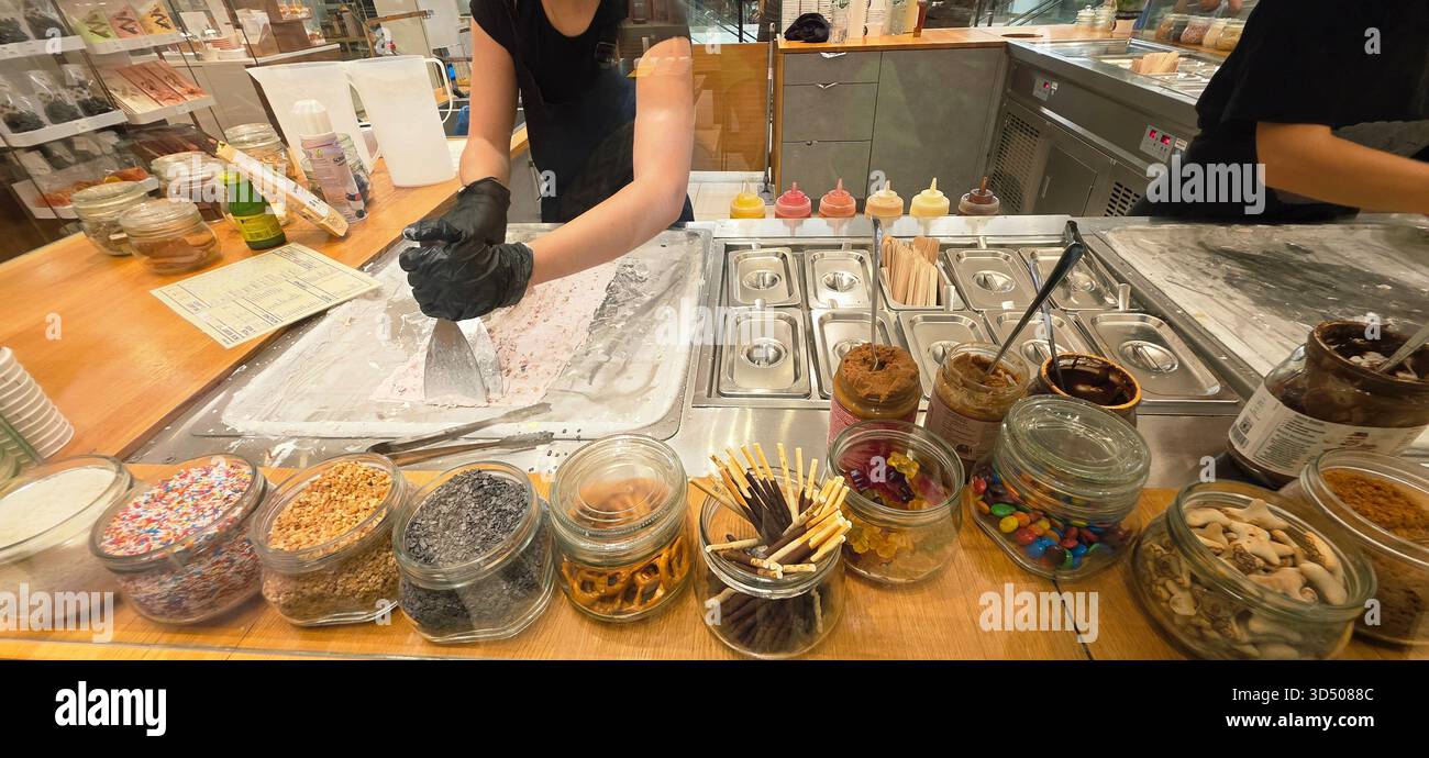 Berlin, Deutschland - 19. September 2025: Mitarbeiter der Eisdiele fertigt Rolleis mit verschiedenen Belägen. - Smartphone-aufgenommenes Stockfoto
