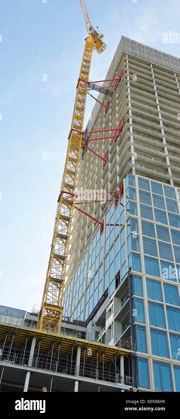 Berlin, Deutschland - 28. September 2025: . Der Baukran ragt über einem modernen Gebäude vor blauem Himmel - Smartphone-aufgenommenes Stockfoto