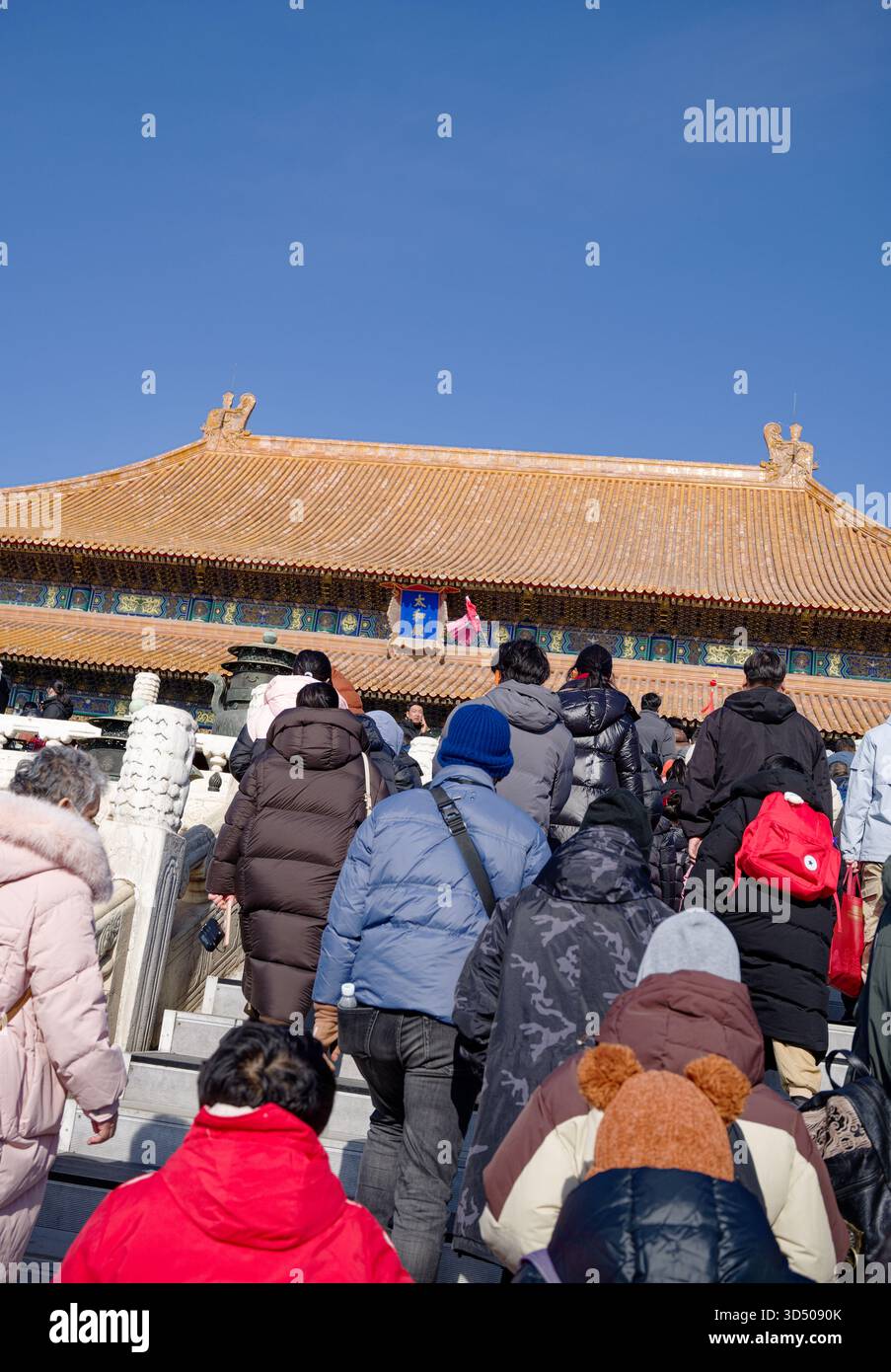 Besucher in Wintermänteln klettern Marmortreppen zu einer verzierten Halle in Pekings Verbotener Stadt unter einem strahlend blauen Himmel Stockfoto