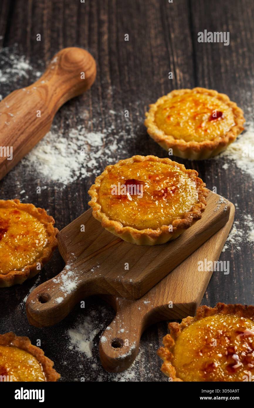 Frisch gebackene Vanillekuchen sitzen auf einem hölzernen Schneidebrett, mit einer goldenen Kruste und einer glatten Füllung. Mehl und eine Nudelnadel ergänzen die gemütliche Küche Stockfoto
