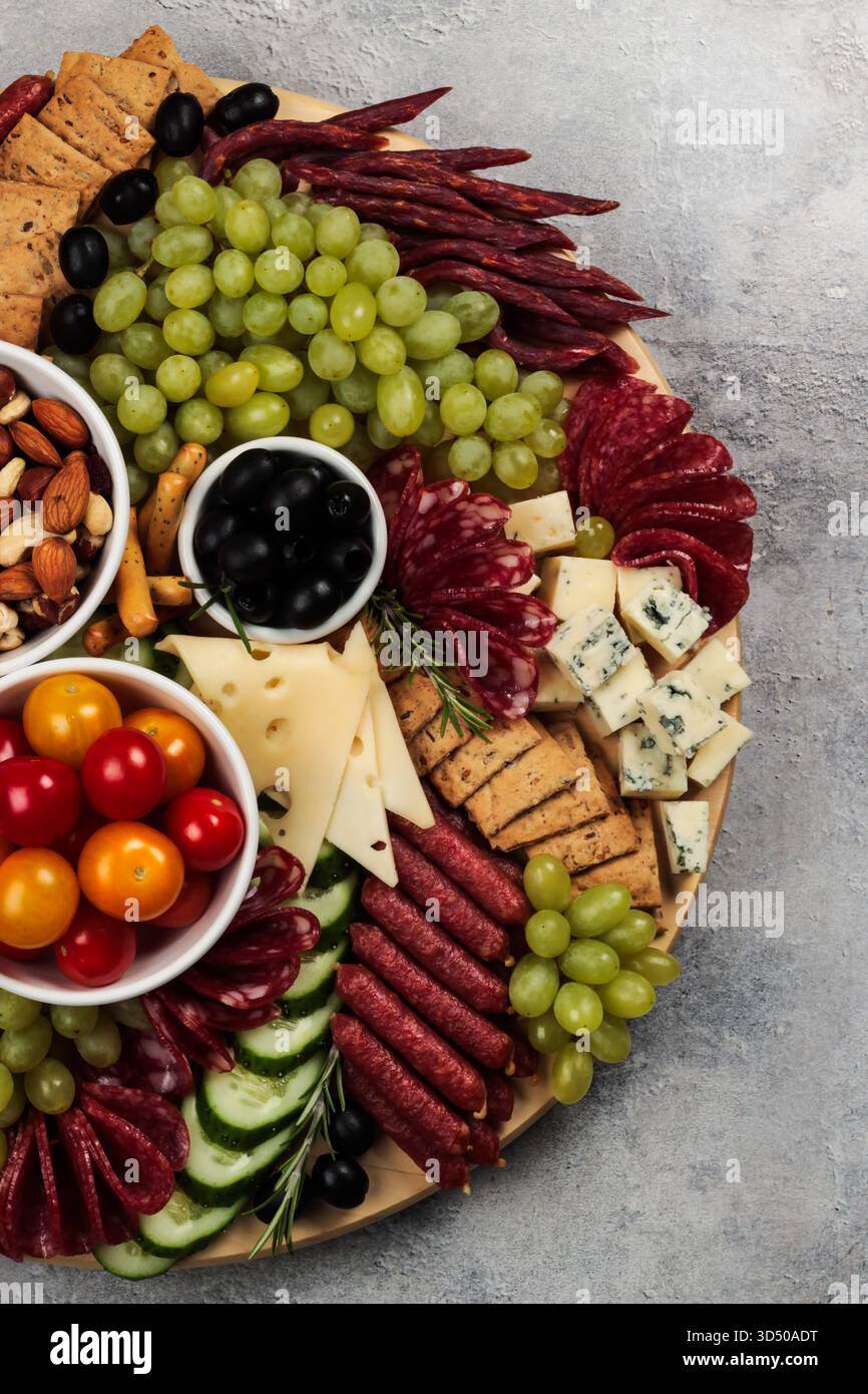 Eine farbenfrohe Wurstplatte ist mit verschiedenen Aufschnitt- und Käsesorten, frischen Trauben, Oliven und Kirschtomaten, perfekt zum Teilen an einem legeren Matt Stockfoto