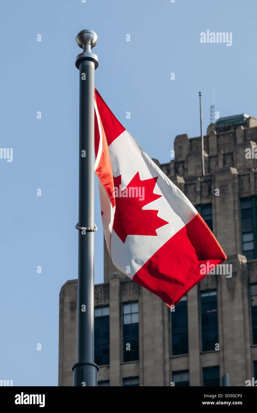 Montreal, Kanada - 11. August 2025: Die kanadische Flagge winkt vor dem historischen Aldred Building am Place d’Armes in Old Montreal Stockfoto