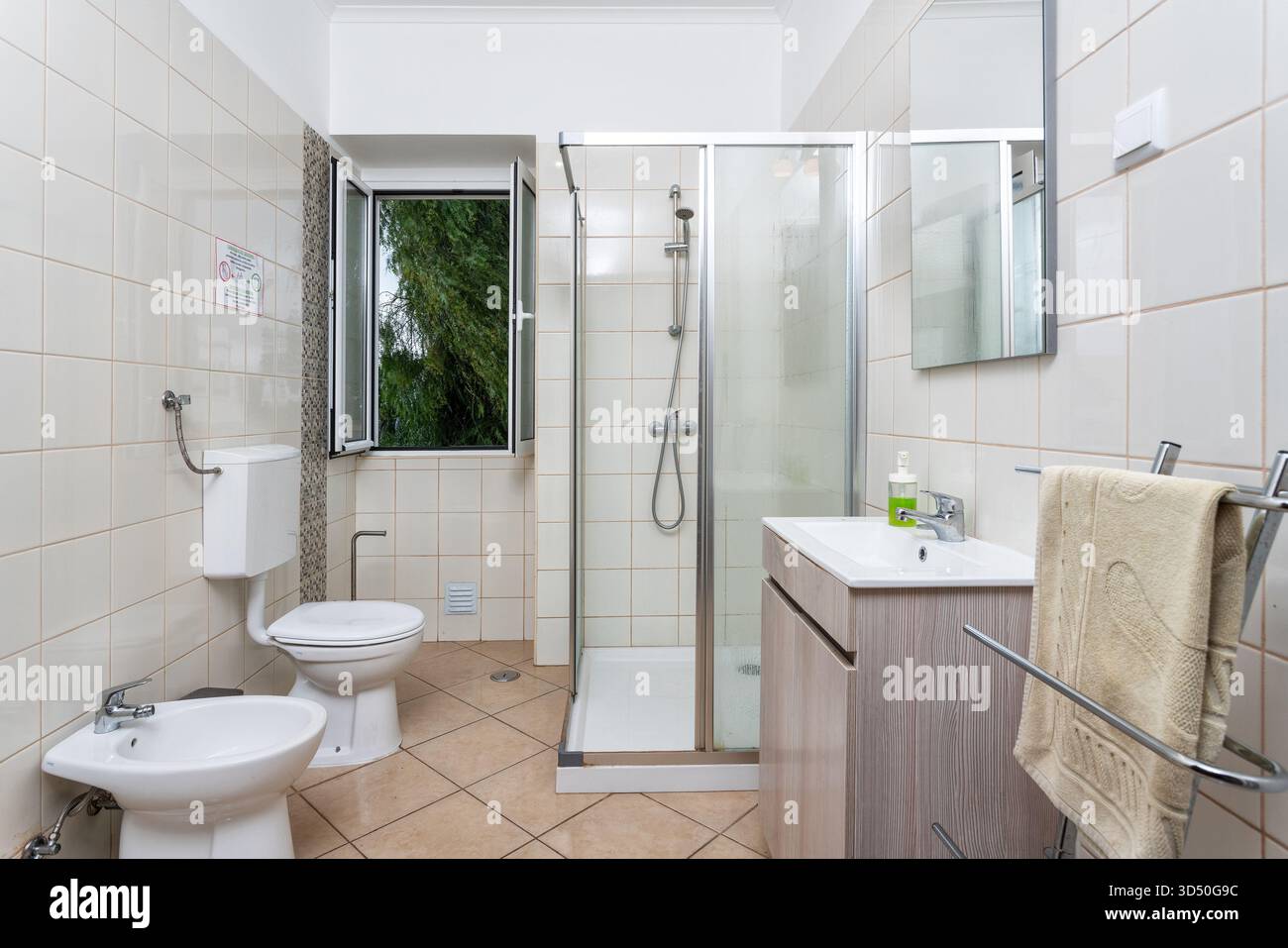 Das moderne Badezimmer verfügt über eine begehbare Dusche, Toilette und Bidet mit großen Fliesen und natürlichem Licht durch das offene Fenster Stockfoto