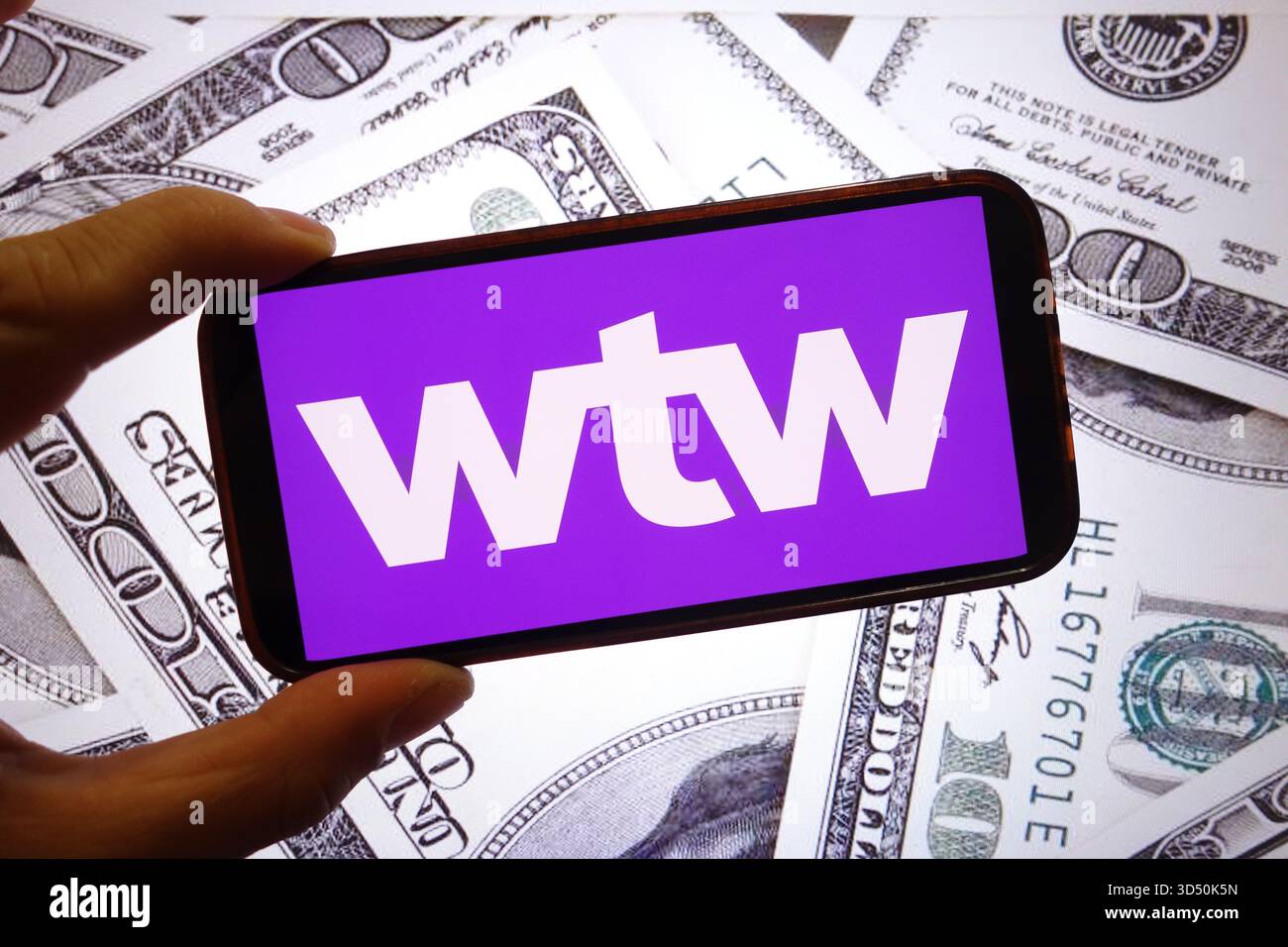 In dieser Fotoabbildung ist das Willis Towers Watson Firmenlogo auf einem Smartphone-Bildschirm mit US-Dollar-Banknoten im Hintergrund zu sehen. Stockfoto