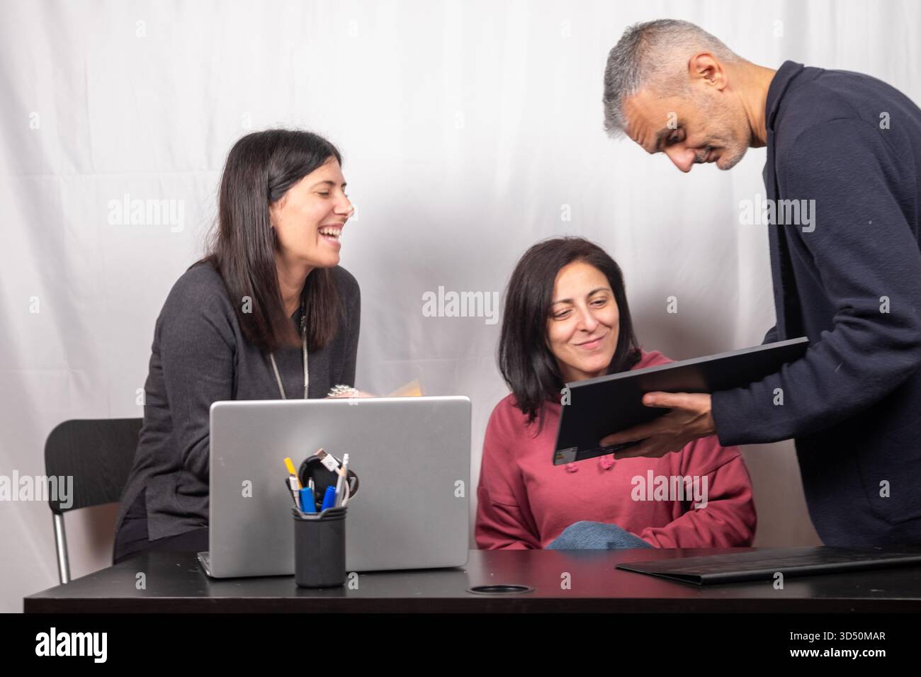 Lachen unter Kollegen während einer Pause vor dem Computer. Die beiden Frauen und der Mann sind vierzig Jahre alt und Italiener Stockfoto
