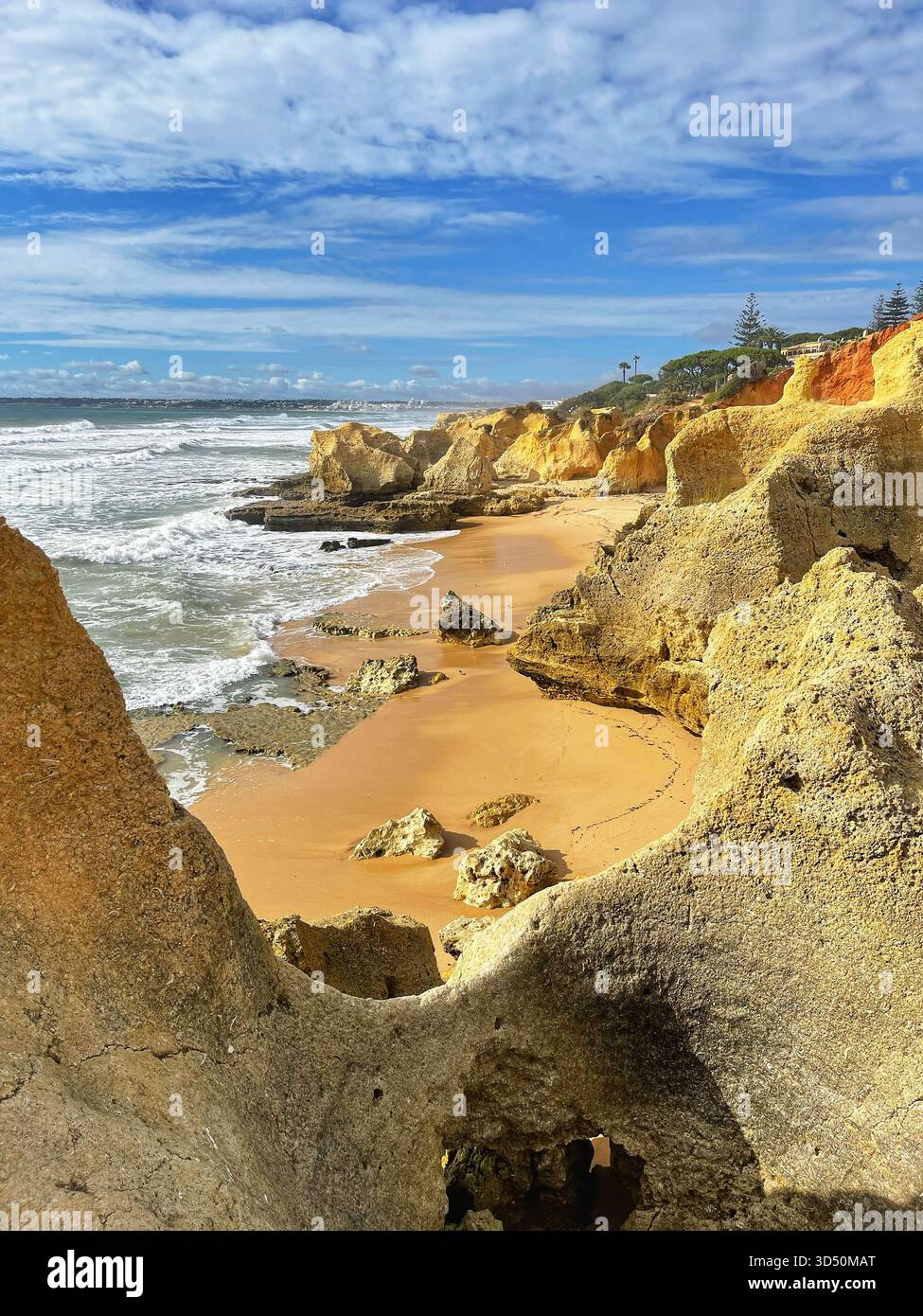 Schaumige Wellen krachen auf den Felsen des abgelegenen Praia dos Bés, Albufeira, unter Klippen und einem lebhaften Himmel voller Wolken Stockfoto