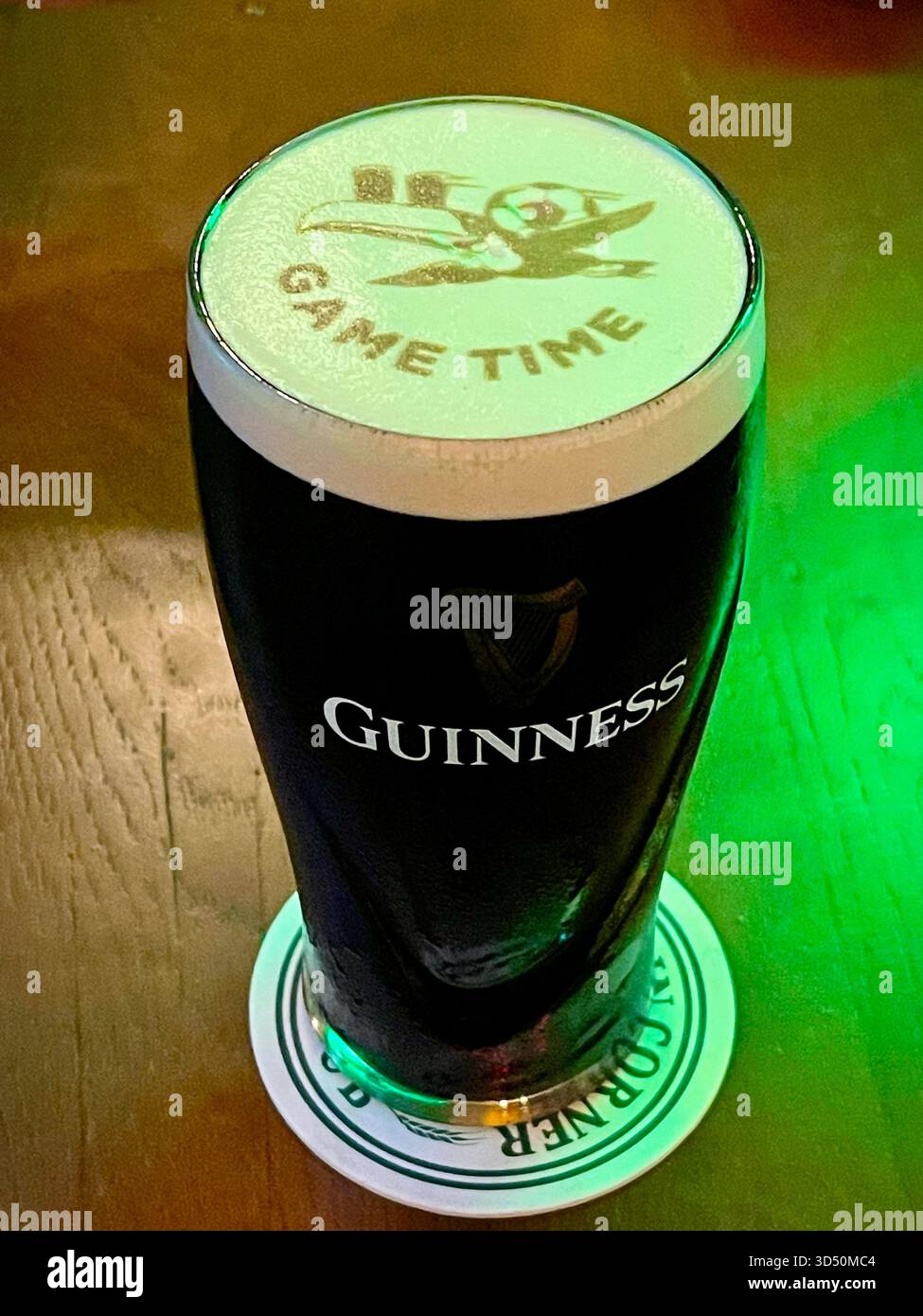 Pint of Guinness mit dem berühmten Tukan-Markenzeichen und „GAME TIME“ auf Schaumstoff, serviert auf der Achterbahn in einem britischen Pub Stockfoto