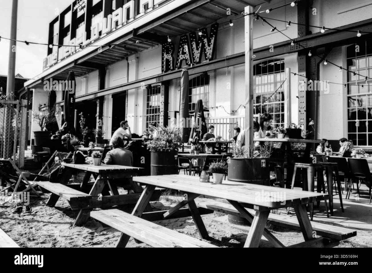 Cafe RAW Terrace. Terrasse und Gäste des Cafe RAW Spoorzone an einem warmen, sonnigen Nachmittag 2023, Tilburg, Niederlande. Aufgenommen mit analogem Schwarzweißfilm, 2023. Tilburg Cafe RAW / Spoorzone 013 Noord-Brabant Nederland Copyright: XGuidoxKoppesxPhotox Stockfoto