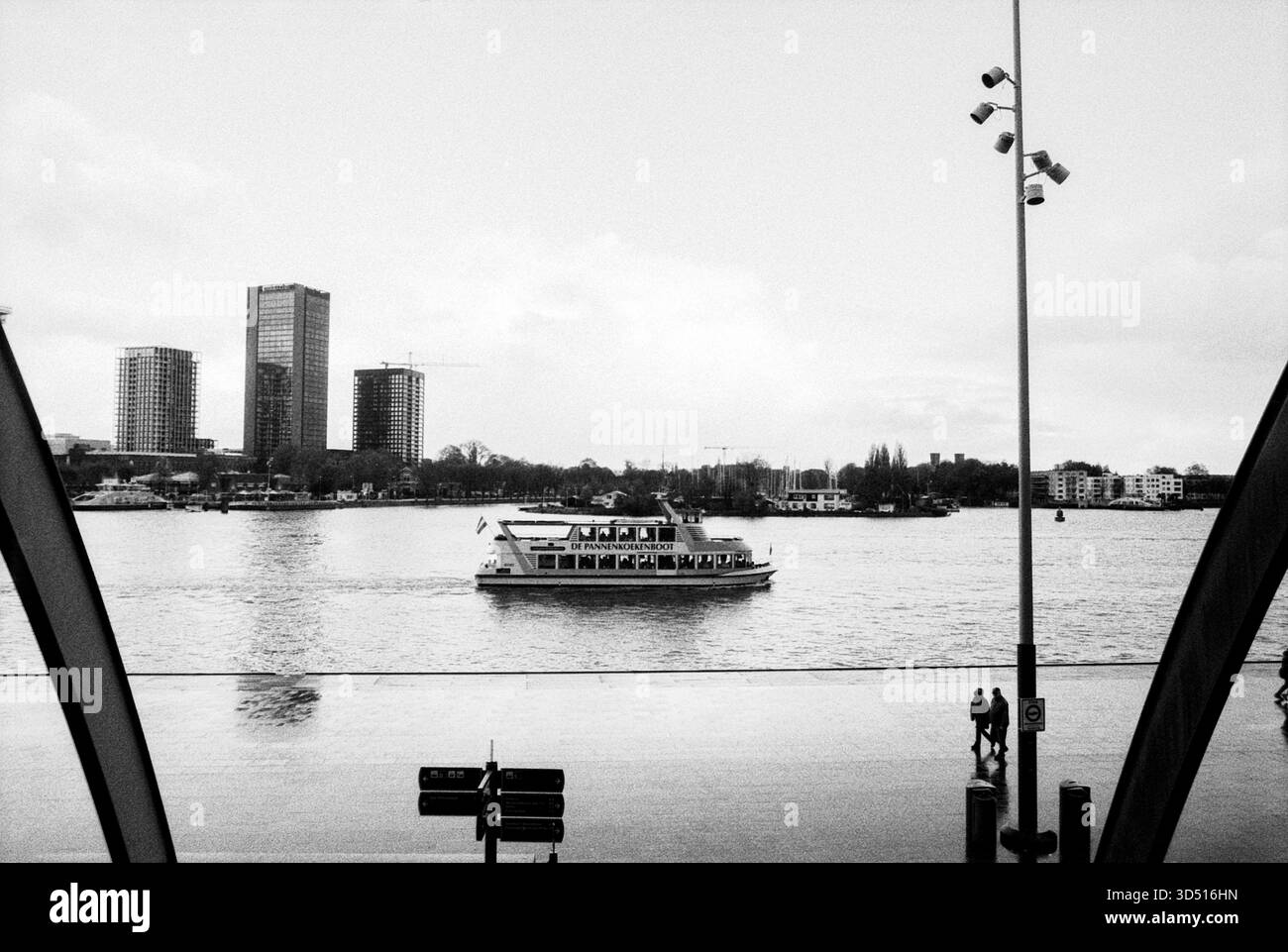 Pfannkuchenboot auf dem IJ River. Blick auf den IJ River und das Pancake Boot vom Hauptbahnhof. Amsterdam, Niederlande. Aufgenommen mit analogem Schwarzweißfilm, 2024. Amsterdam Centraal Station Noord-Holland Nederland Copyright: XGuidoxKoppesxPhotox Stockfoto