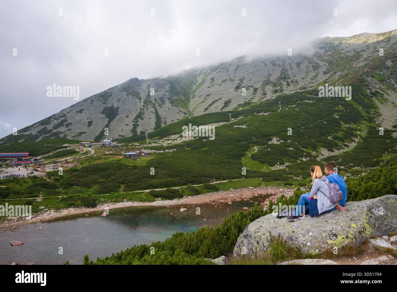 Ein Paar sitzt auf einem Felsen neben Skalnaté Pleso, einem wunderschönen Bergsee in der hohen Tatra. Stockfoto