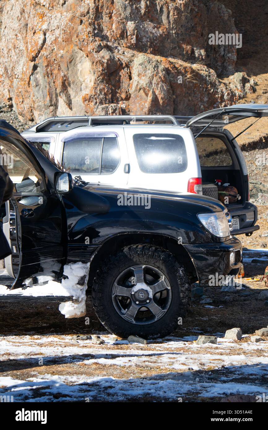 Naryn, Kirgisistan – 12. November 2025: Seitenansicht eines schwarzen Toyota Land Cruiser 100, der neben einem weißen SUV geparkt ist, mit dem Kofferraum des weißen SUV Stockfoto