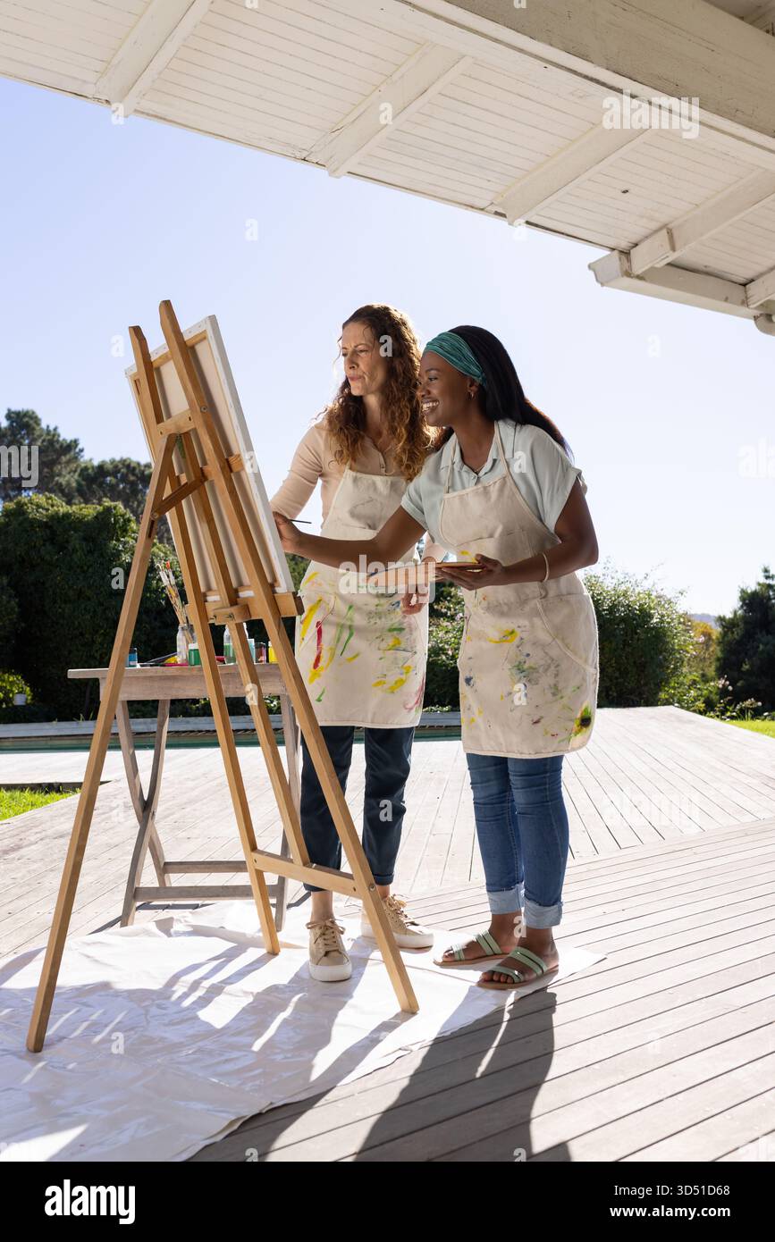 Malerei verschiedener weiblicher Freunde, die auf Leinwand auf der Veranda an der Staffelei zusammenarbeiten, mit Farbpalette Stockfoto
