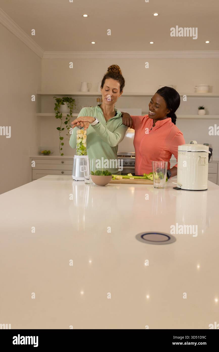 Gemischte weibliche Freunde, die Smoothie auf der Kücheninsel zubereiten, mit Mixer und Schneidebrett Stockfoto