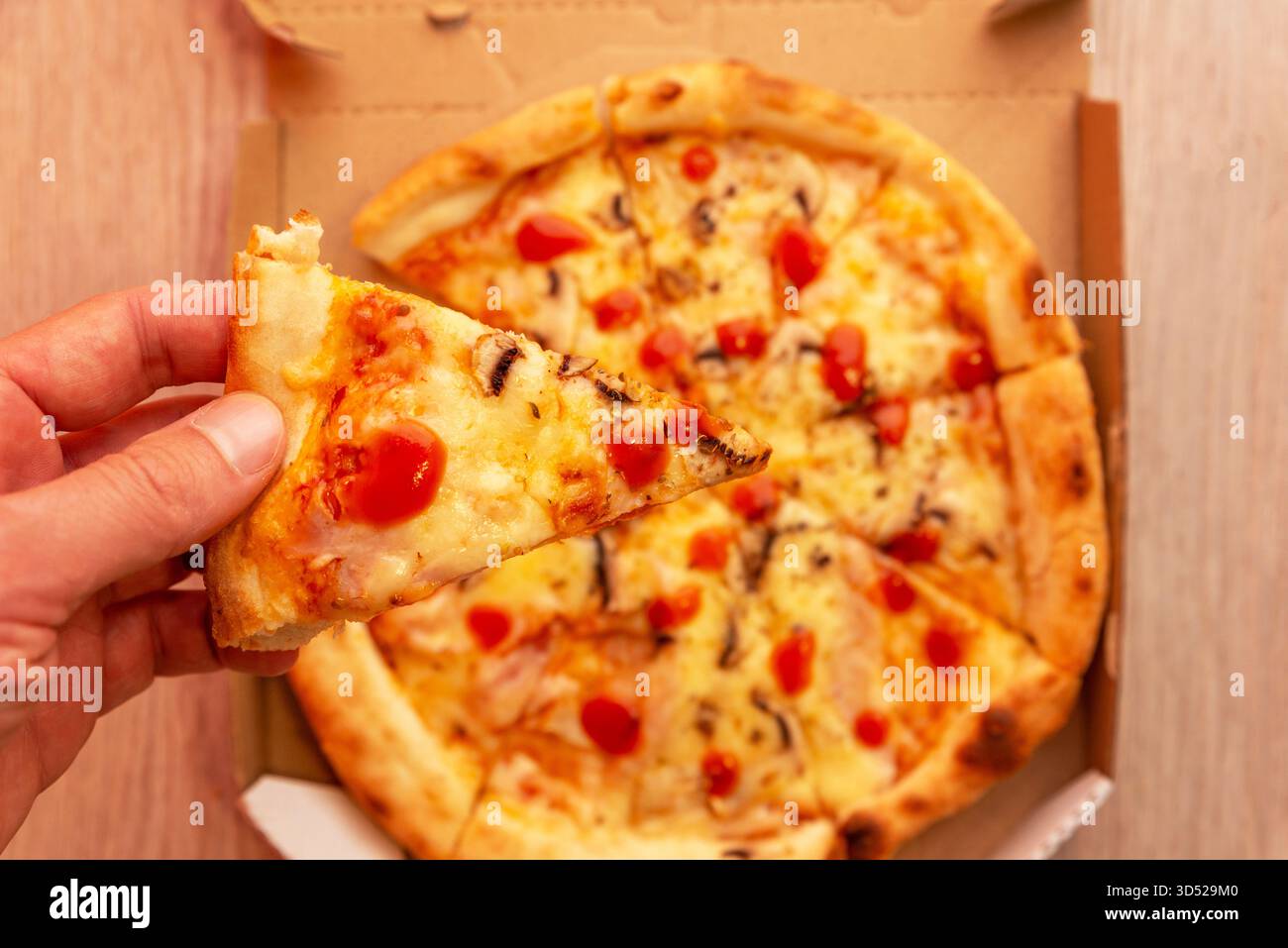 Halten Sie ein Stück frischer Pizza von Hand über dem offenen Lieferkarton mit geschmolzenem Käse und Tomatensauce, Konzept für Fast Food und zwangloses Essen Stockfoto