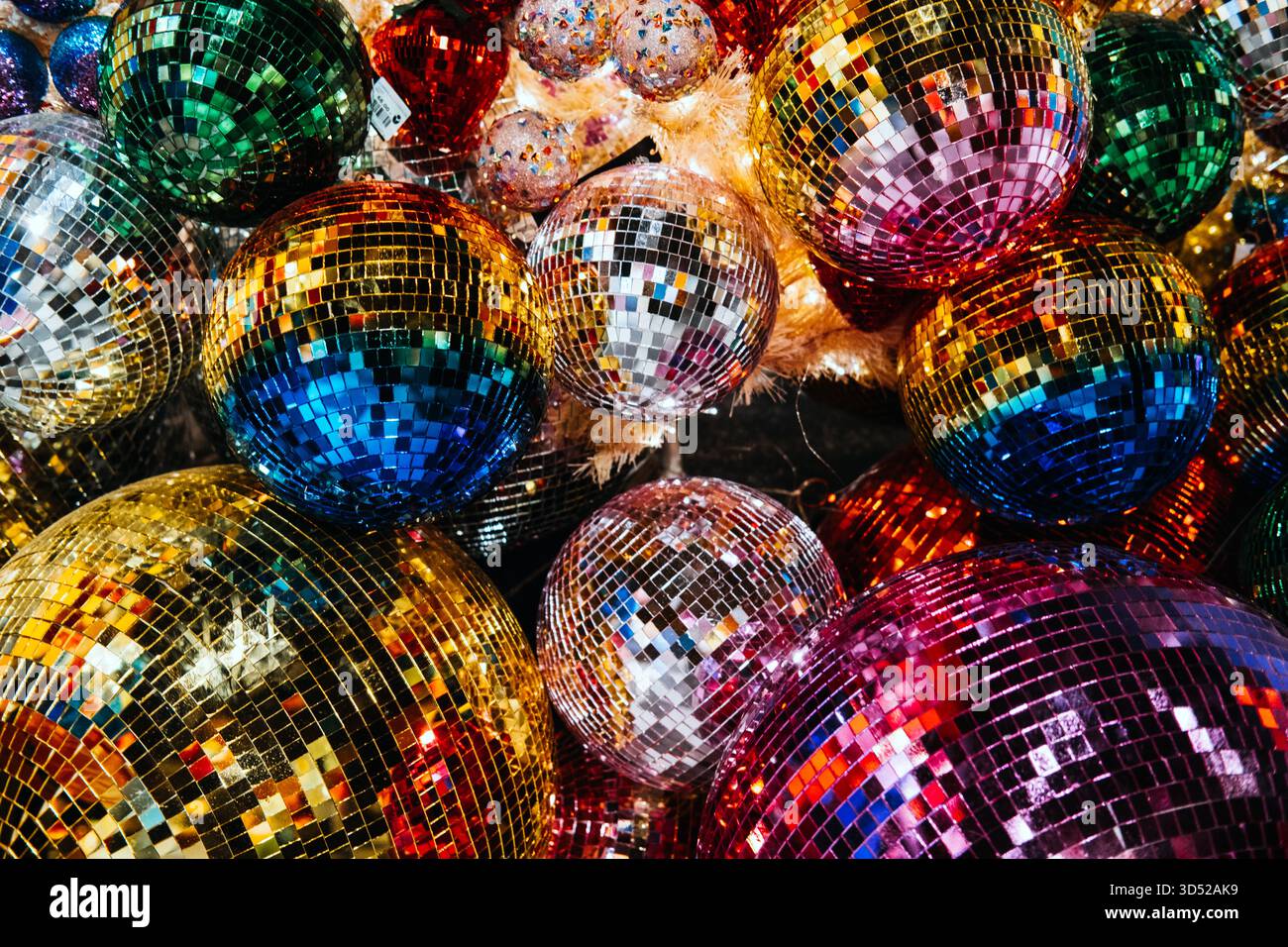 Ein lebhafter Haufen übergroßer Disco-Ball-Ornamente in Regenbogenform in festlichen Festtagen auf einem karierten Boden. Regenbogenschmuck, LGBTQ-Feiertage, Stolz Stockfoto
