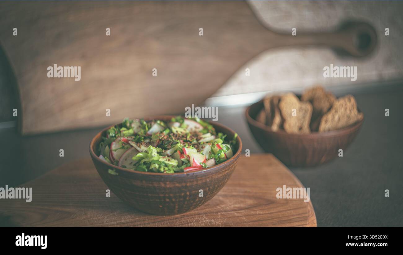 Frischer Marktsalat mit Radieschen, Gurken und grünen Kräutern, serviert in einer rustikalen Tonschale auf einem hölzernen Schneidebrett. Natürliches Licht hebt lebendige Akzente Stockfoto