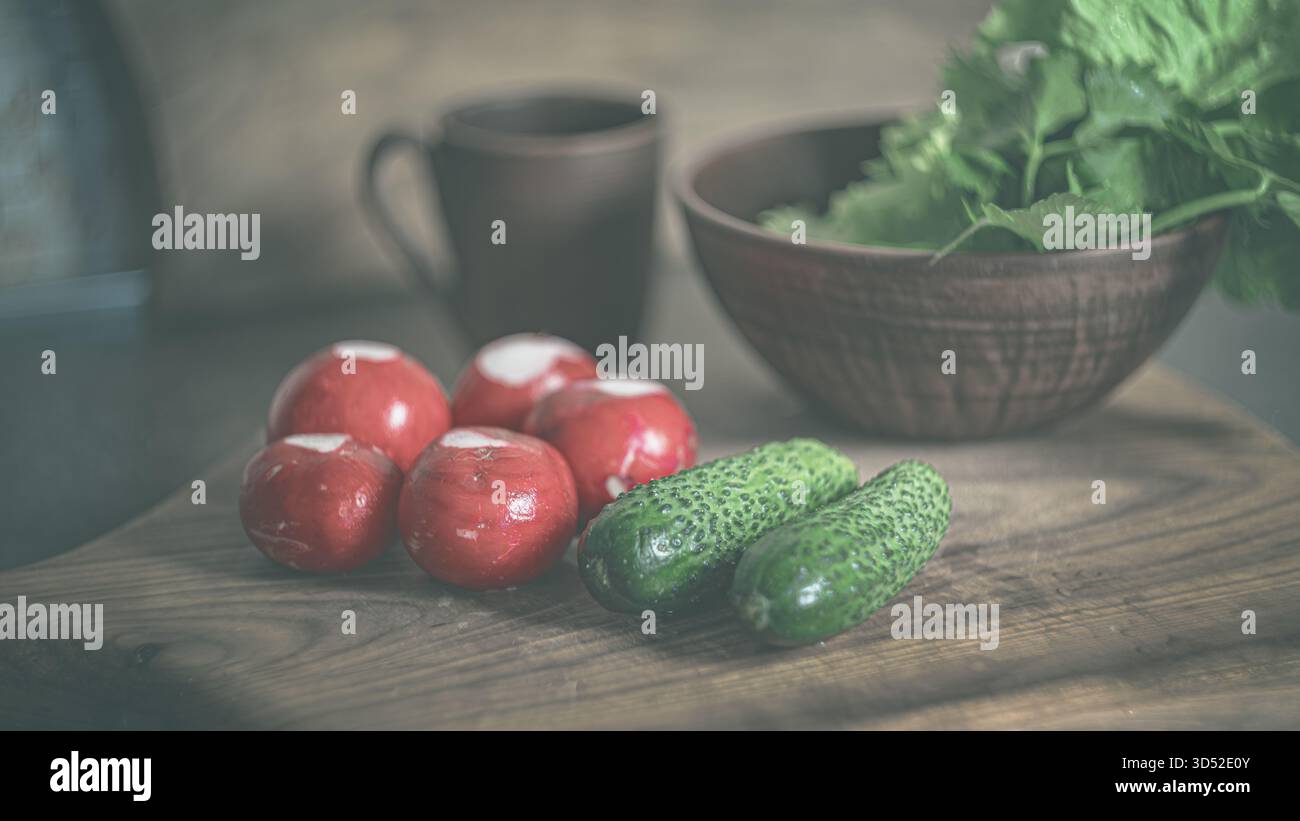 Frisch geerntete Radieschen, Gurken und grüne Kräuter vom Markt auf einem rustikalen Küchentisch. Natürliche Texturen und leuchtende Farben heben hervor Stockfoto