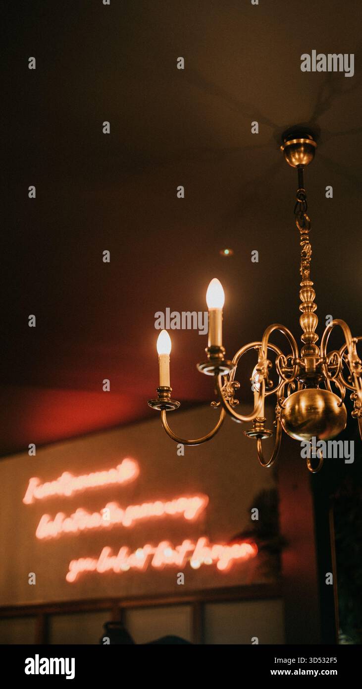 Ein Neonschild mit der Aufschrift „du bist nicht allein“ leuchtet hell in einem schwach beleuchteten Raum. Das Schild ist von drei Kerzen umgeben, die ein warmes Licht erzeugen Stockfoto