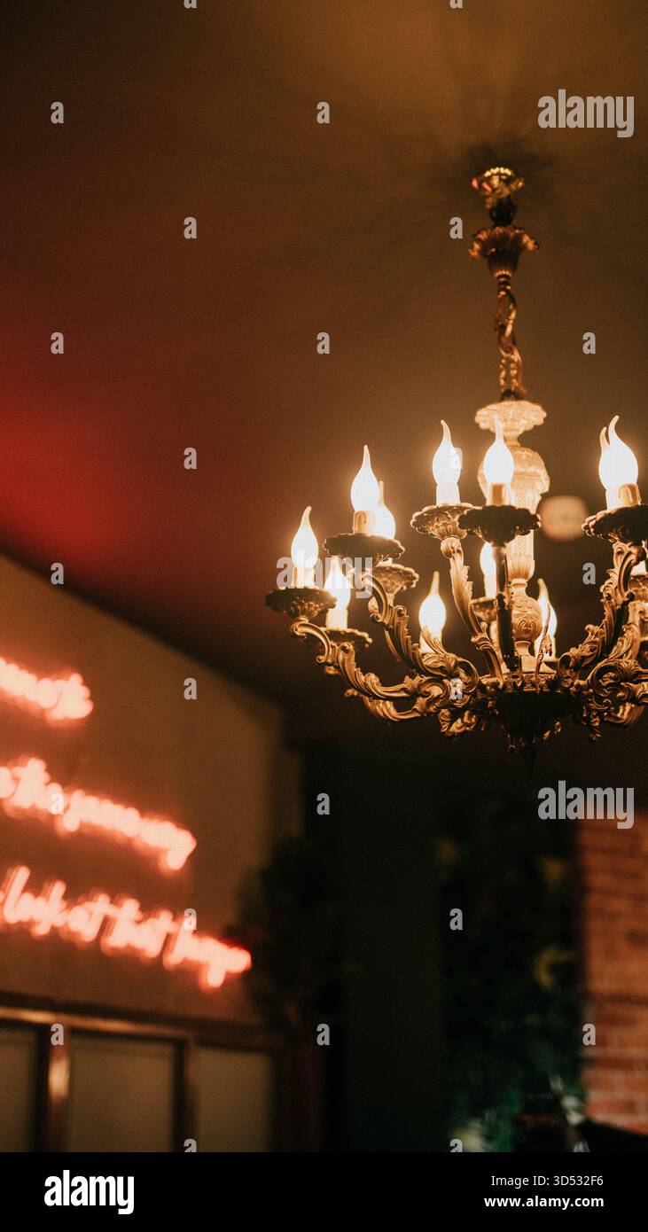 In einem schwach beleuchteten Raum hängt ein Kronleuchter von der Decke. Der Kronleuchter ist mit einem roten Neonschild beleuchtet, auf dem steht: "Stärker als die Reise deines l Stockfoto