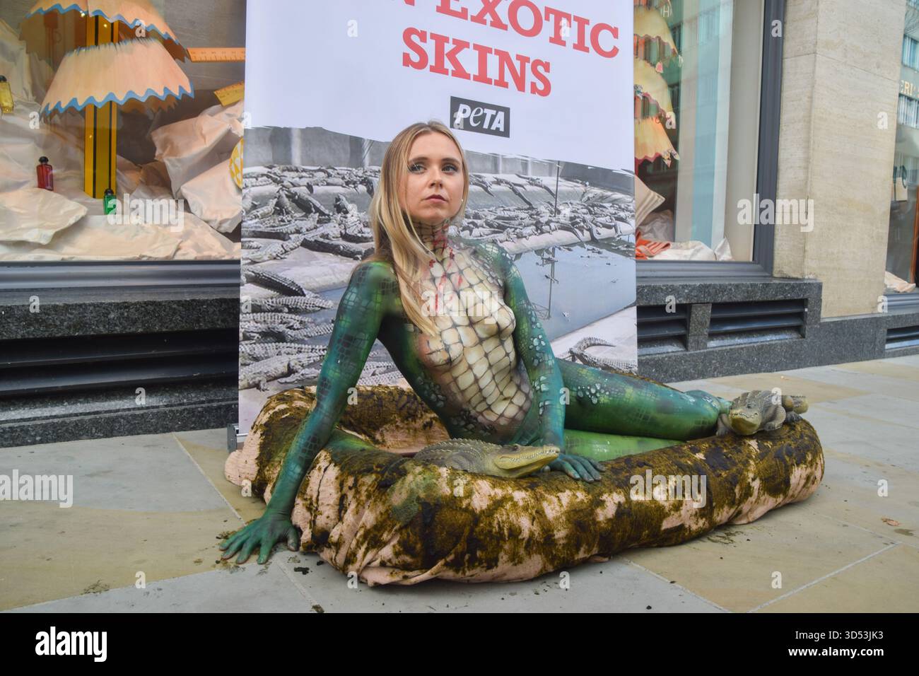 London, Großbritannien. November 2025. Ein PETA-Aktivist mit Krokodilfarbe liegt in einem „dreckigen“ Pool außerhalb von Hermes in der New Bond Street, während die Tierschutzgruppe gegen die Verwendung von Krokodilen und anderen exotischen Häuten durch die Luxusmarke protestiert. Quelle: Vuk Valcic/Alamy Live News Stockfoto