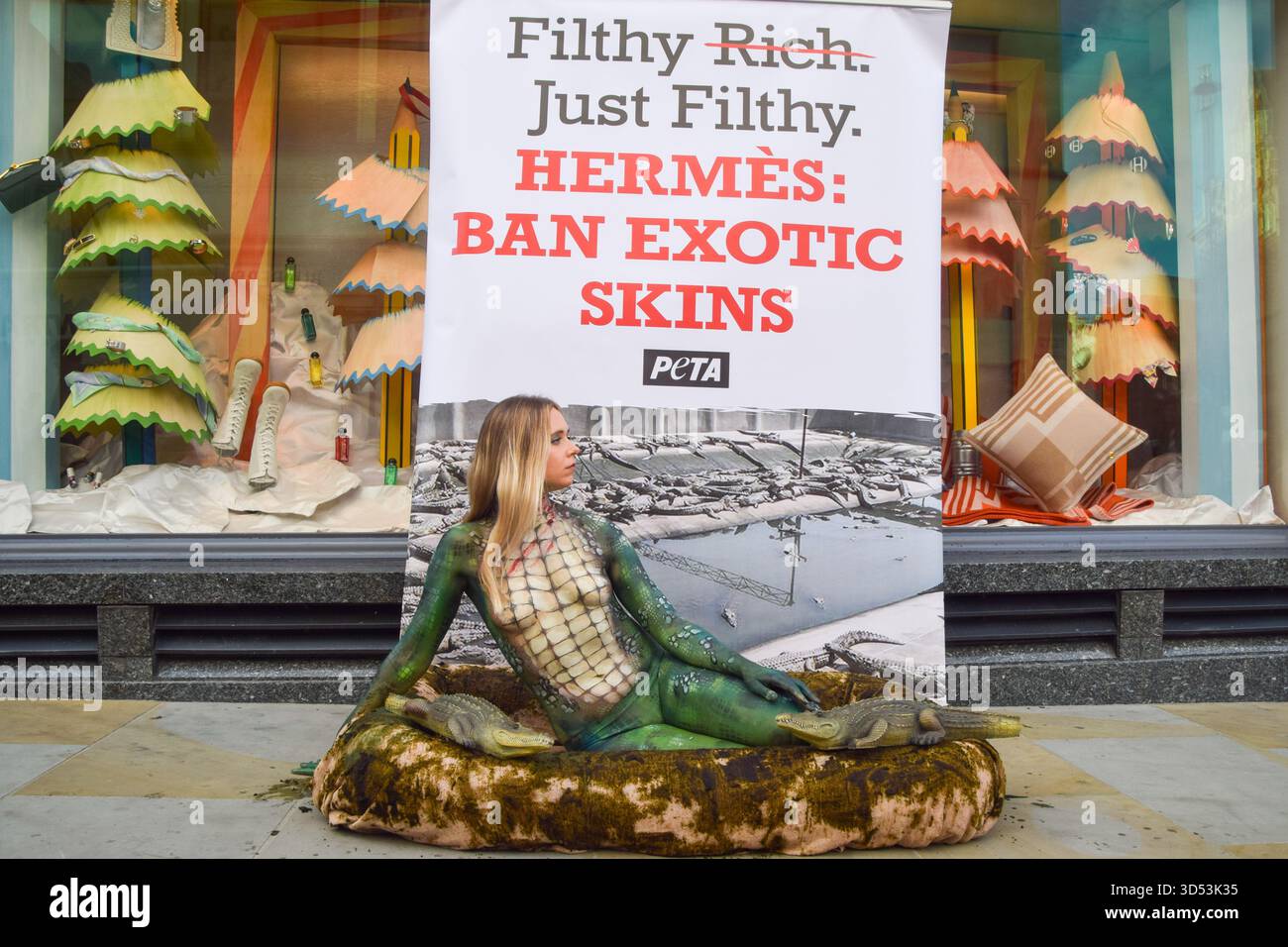 London, Großbritannien. November 2025. Ein PETA-Aktivist mit Krokodilfarbe liegt in einem „dreckigen“ Pool außerhalb von Hermes in der New Bond Street, während die Tierschutzgruppe gegen die Verwendung von Krokodilen und anderen exotischen Häuten durch die Luxusmarke protestiert. Quelle: Vuk Valcic/Alamy Live News Stockfoto