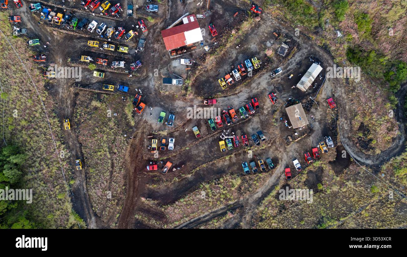 Aus der Vogelperspektive eines Fahrzeugfriedhofs mit einer Mischung aus bunten Autos und Lastwagen, die in der dunklen Erde in der Nähe des Mount Batur, Bali, Indonesien, verstreut sind. Stockfoto