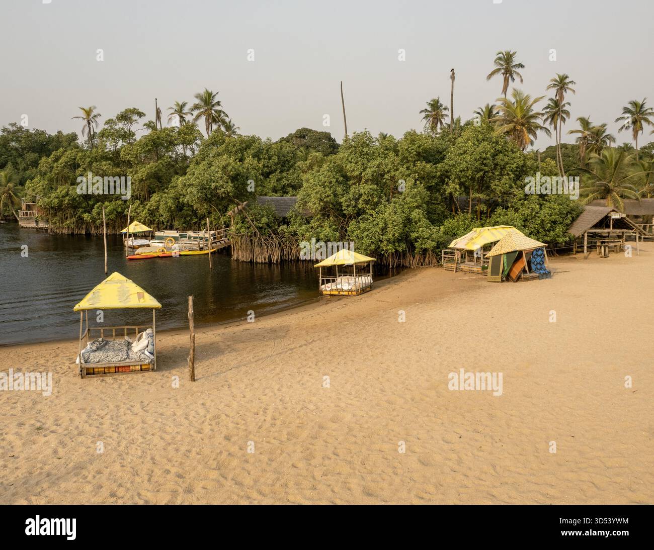 Blick aus der Vogelperspektive auf einen ruhigen Fluss, der auf üppige grüne Vegetation mit Gebäuden inmitten von Bäumen trifft, Lagos, Nigeria. Stockfoto