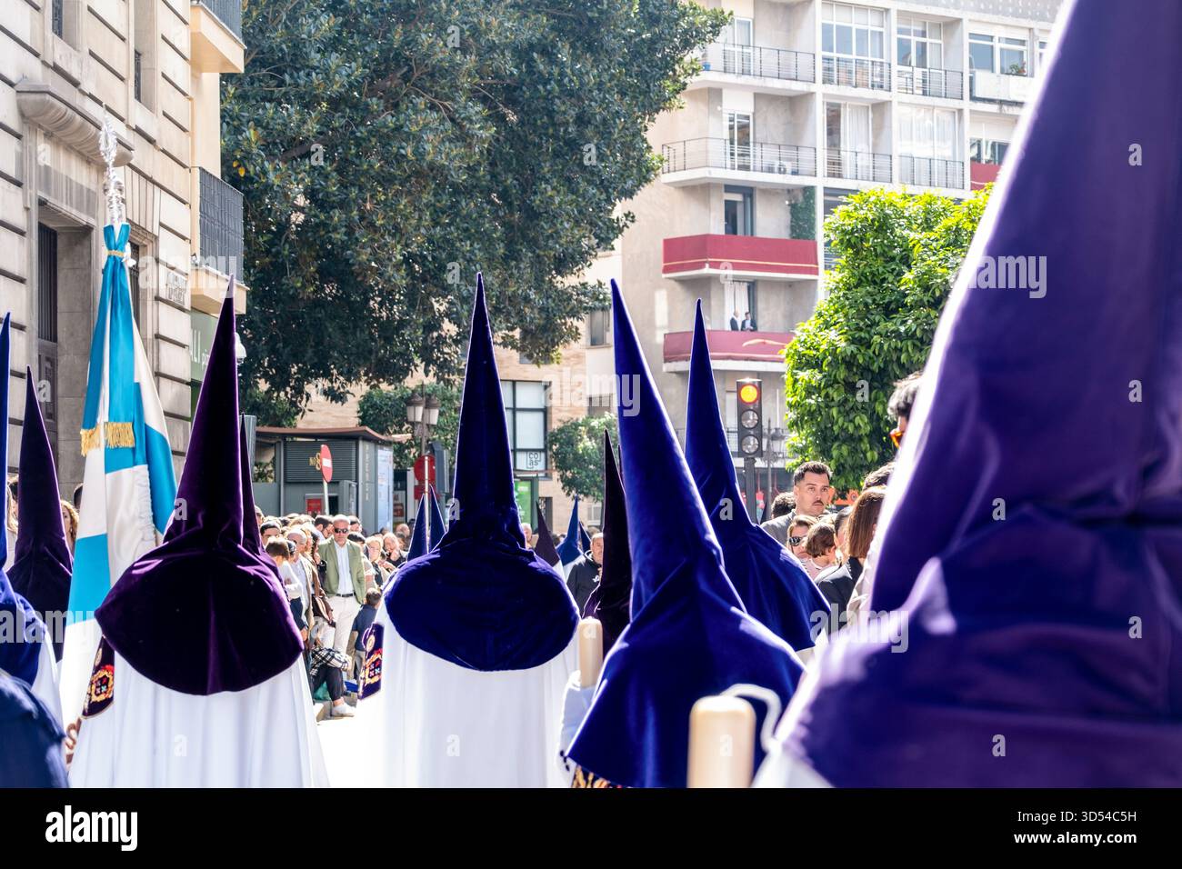 Ostersemana Santa Prozession in Sevilla, Spanien, 15. April 2025. Nazarenos in weißen Gewändern und violetten Kapuzen spazieren durch historische Straßen, umgeben von ihnen Stockfoto