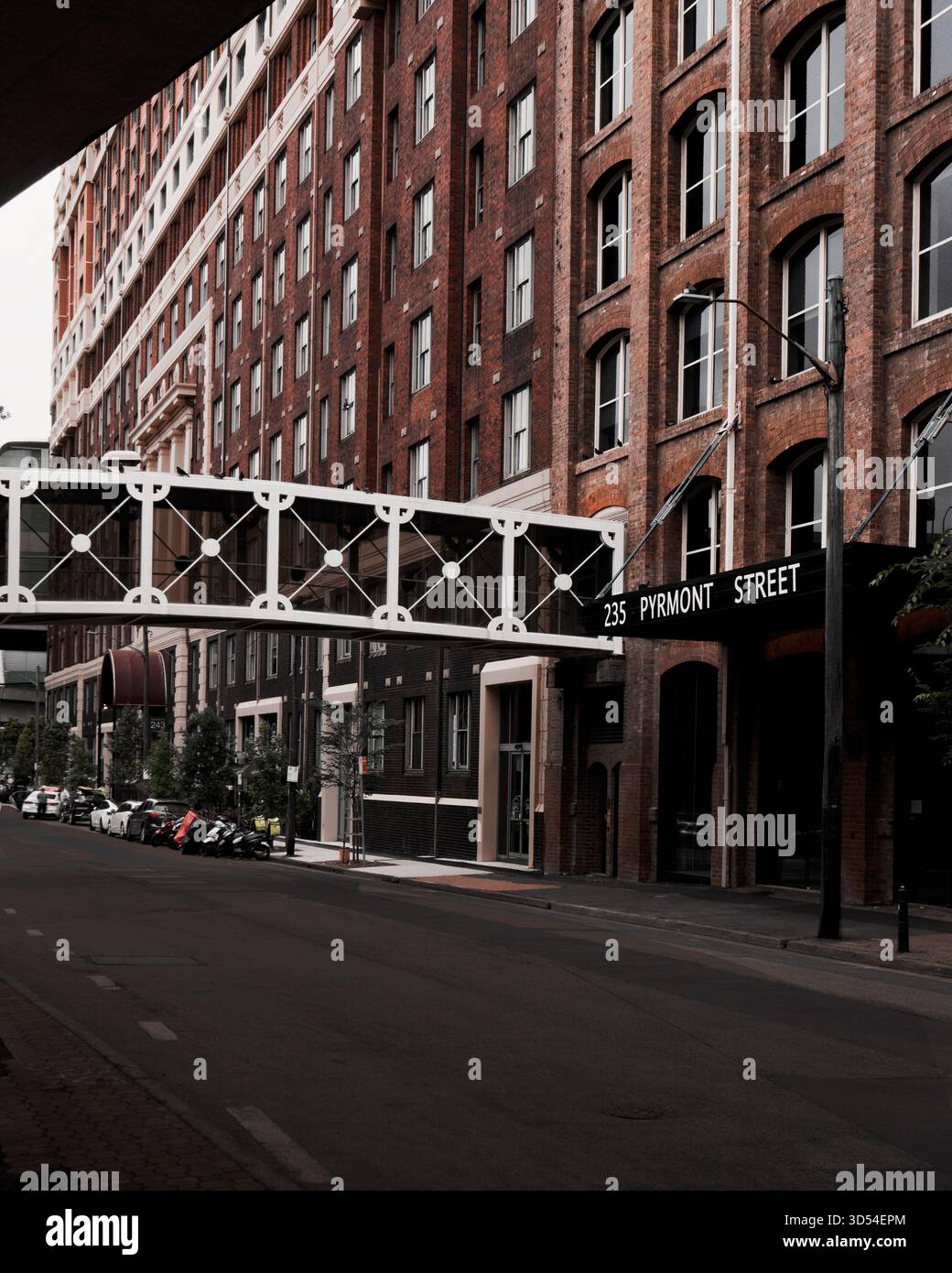 Eine ruhige Stadtstraße, die von traditionellen Backsteinbauten und einer weißen Fußgängerbrücke eingerahmt wird. Ideal für Themen wie Architektur, Stadtdesign, Immobilien. Stockfoto