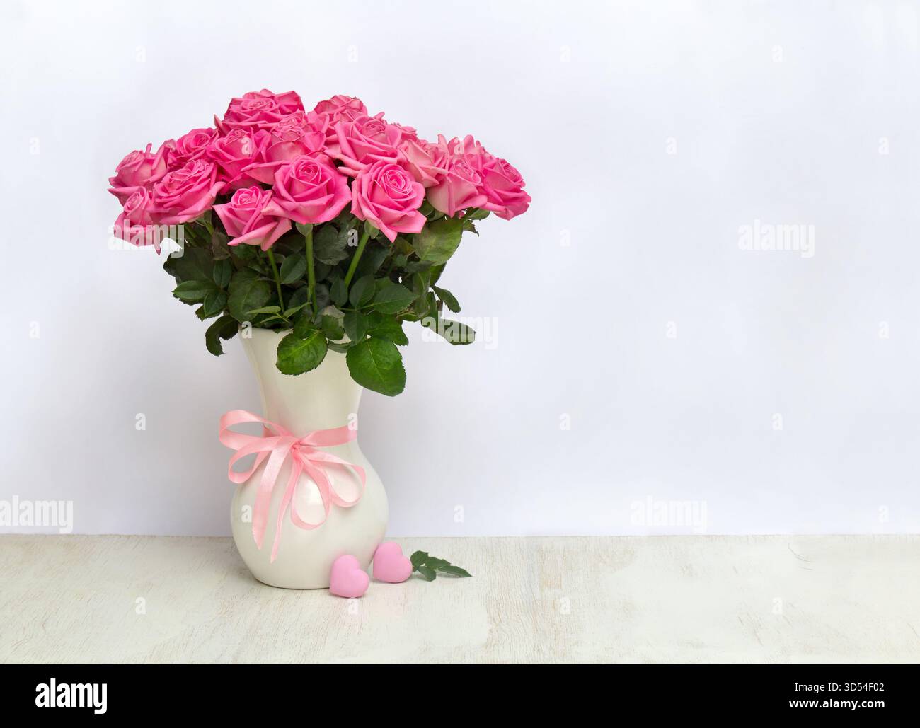 Strauß rosa Blumen Rosen in einer weißen Porzellanvase und rosa Herzen auf einem weißen Tisch auf hellem Hintergrund mit Platz für Text Stockfoto