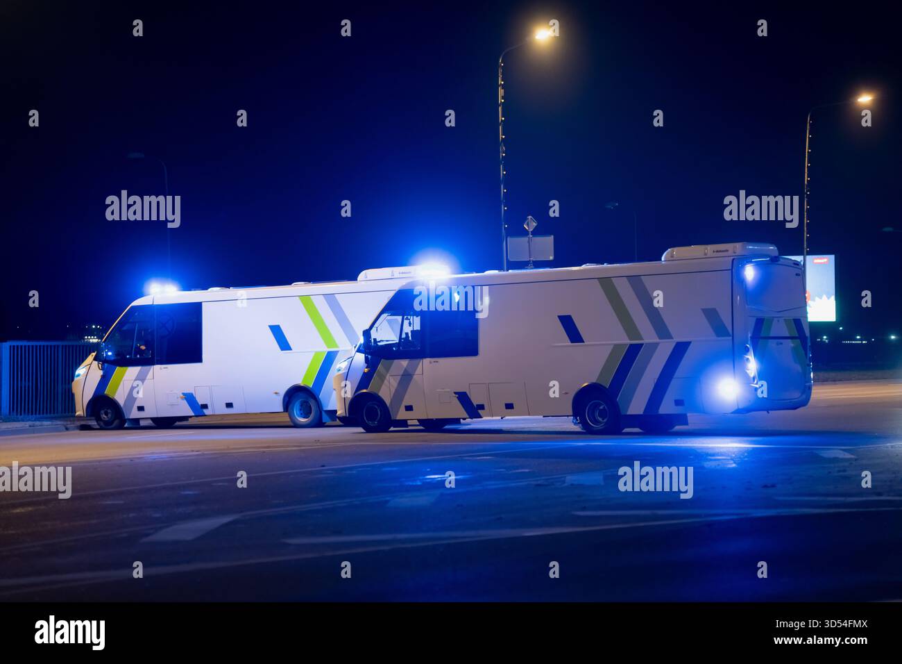 Zwei Polizeifahrzeuge mit aktivem blauem Licht, die nachts auf einer leeren Fahrbahn stehen und reflektierende Markierungen, Einsatzbereitschaft und die zeigen Stockfoto