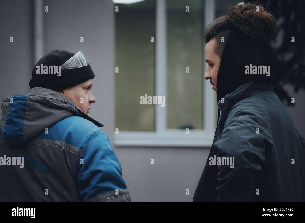 Zwei Männer in Winterarbeitskleidung diskutieren über ein Projekt in der Nähe einer Baustelle. Kaltes Wetter und Teamwork-Atmosphäre bei der Arbeit im Freien. Stockfoto