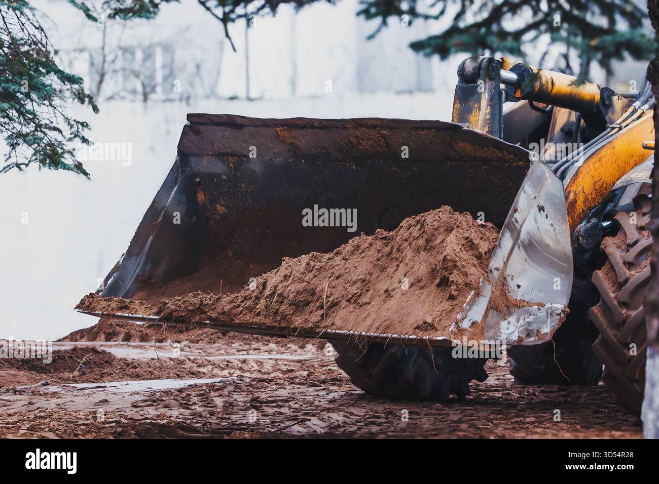 Bagger mit einem Eimer voller Erde, der auf einer Baustelle arbeitet. Schlamm, Maschinen und harte Arbeit vermitteln die Atmosphäre echter Bauarbeiter. Stockfoto